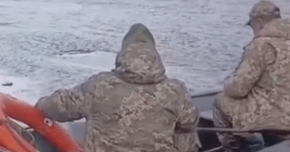 Двоє чоловіків у військовій формі у моторному човні на воді та група людей, які сваряться з ними з берега